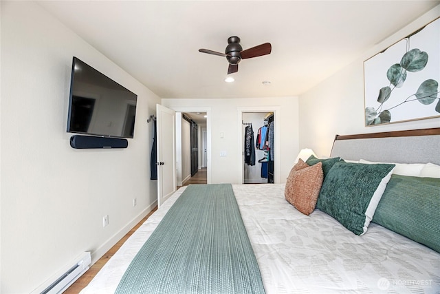 bedroom with a spacious closet, baseboards, a baseboard radiator, a ceiling fan, and wood finished floors