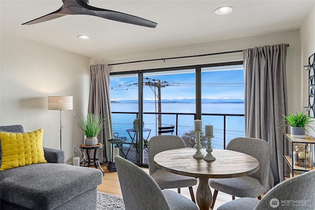 dining room featuring a ceiling fan, a water view, light wood finished floors, and recessed lighting
