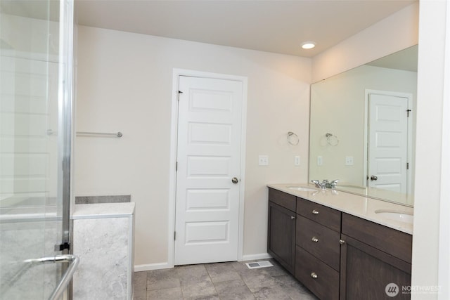 bathroom featuring double vanity, baseboards, a shower with shower door, and visible vents