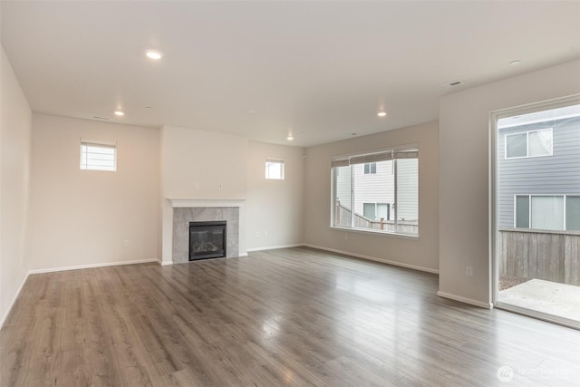 unfurnished living room with a tiled fireplace, recessed lighting, wood finished floors, and a healthy amount of sunlight