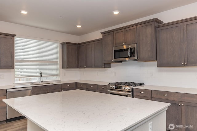 kitchen featuring dark brown cabinetry, a sink, stainless steel appliances, tasteful backsplash, and a kitchen island