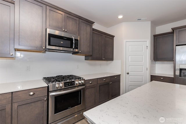 kitchen with dark brown cabinets, light stone counters, stainless steel appliances, backsplash, and visible vents