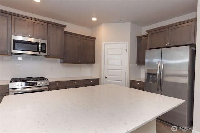 kitchen featuring backsplash, visible vents, appliances with stainless steel finishes, light stone countertops, and dark brown cabinets