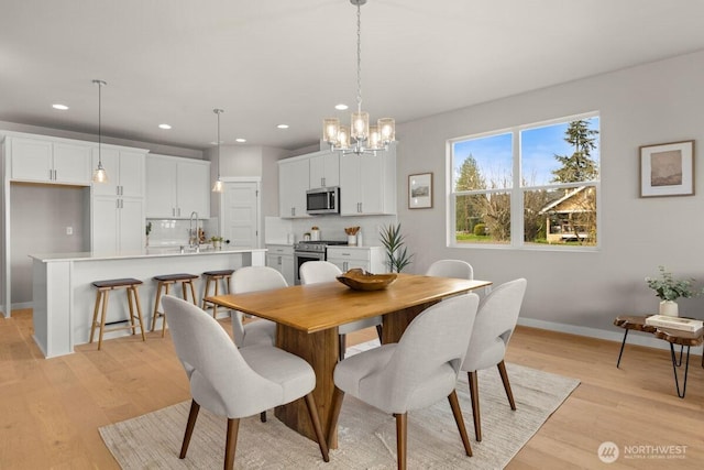 dining space featuring light wood-style floors, baseboards, recessed lighting, and a notable chandelier