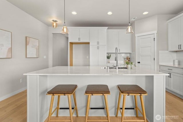 kitchen featuring white cabinets, decorative backsplash, a sink, and light wood-style floors