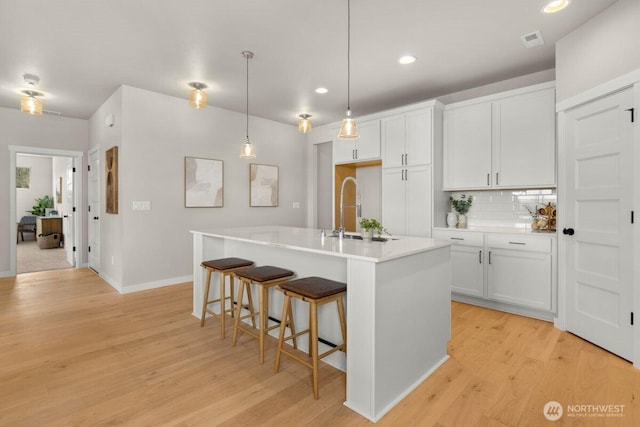 kitchen with a sink, tasteful backsplash, light wood-type flooring, baseboards, and visible vents