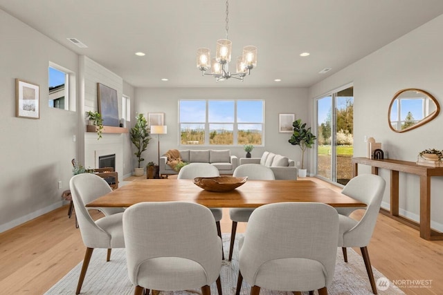 dining room featuring baseboards, visible vents, an inviting chandelier, light wood-style floors, and a fireplace