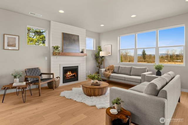 living area featuring recessed lighting, plenty of natural light, visible vents, light wood-type flooring, and a fireplace