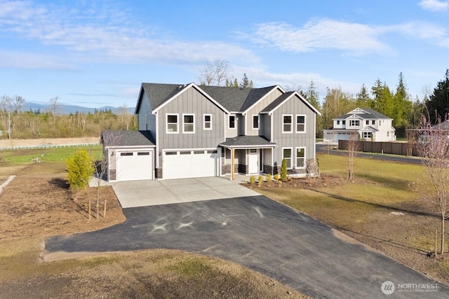 view of front of house featuring a front lawn, driveway, board and batten siding, fence, and a garage