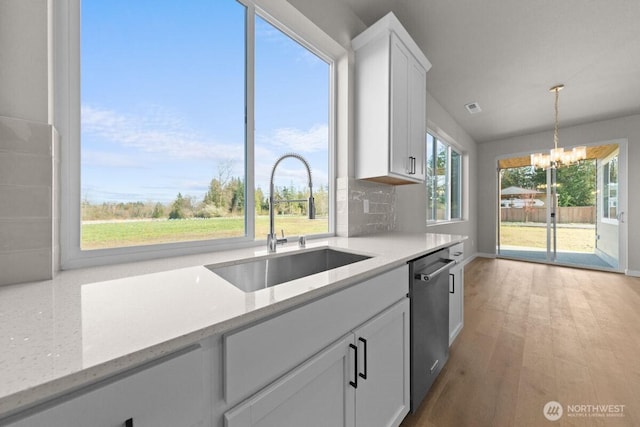 kitchen with stainless steel dishwasher, a sink, an inviting chandelier, white cabinetry, and pendant lighting