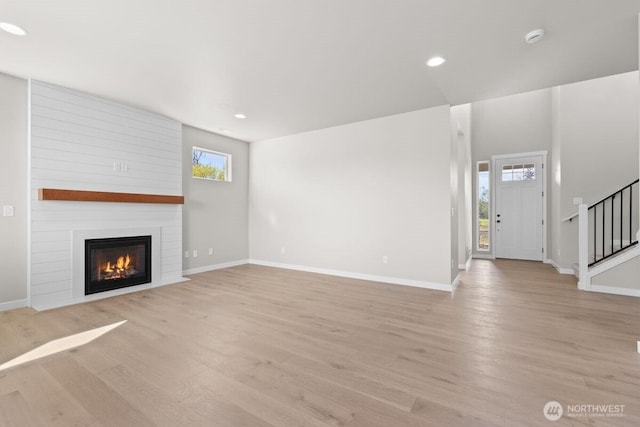 unfurnished living room featuring baseboards, stairs, light wood-style floors, and a fireplace