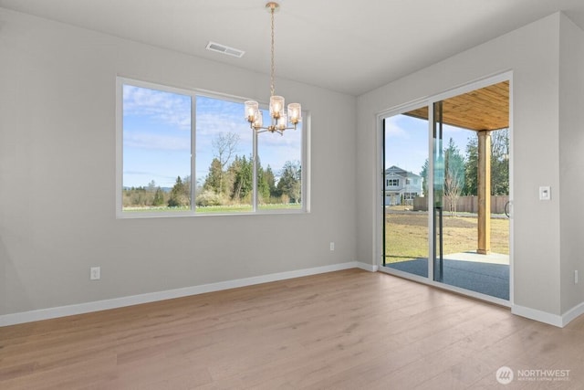 empty room featuring visible vents, light wood finished floors, baseboards, and a notable chandelier
