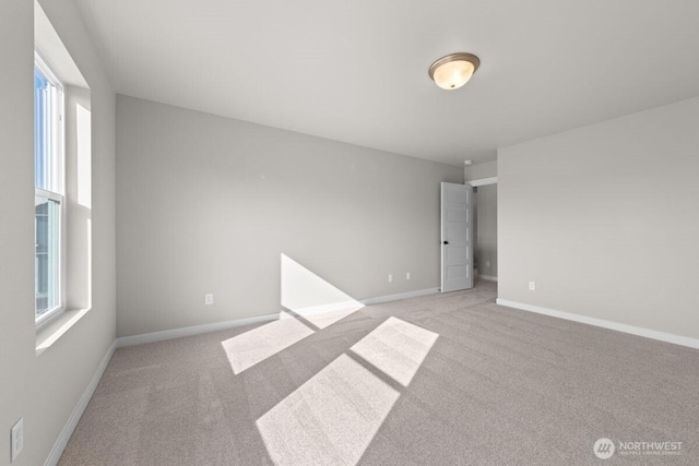 empty room featuring light colored carpet, baseboards, and plenty of natural light