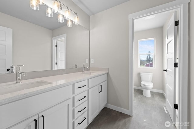 full bathroom featuring toilet, a sink, double vanity, and baseboards