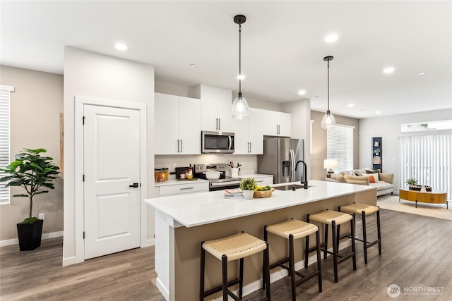 kitchen featuring a breakfast bar, stainless steel appliances, white cabinetry, a center island with sink, and dark wood-style flooring