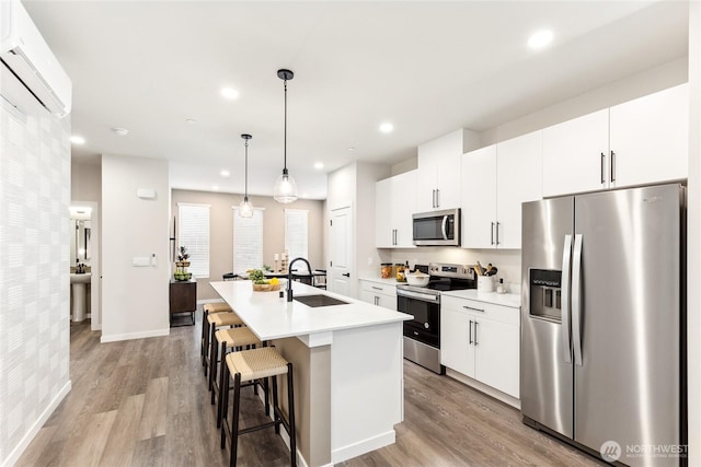 kitchen with a sink, stainless steel appliances, an island with sink, a wall mounted AC, and light wood-style floors
