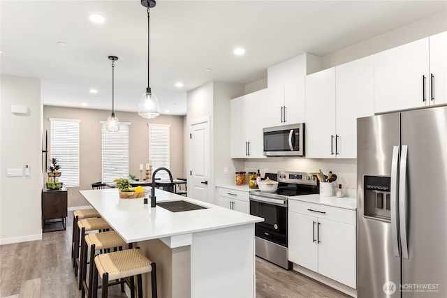 kitchen with light wood finished floors, a kitchen island with sink, stainless steel appliances, and a sink