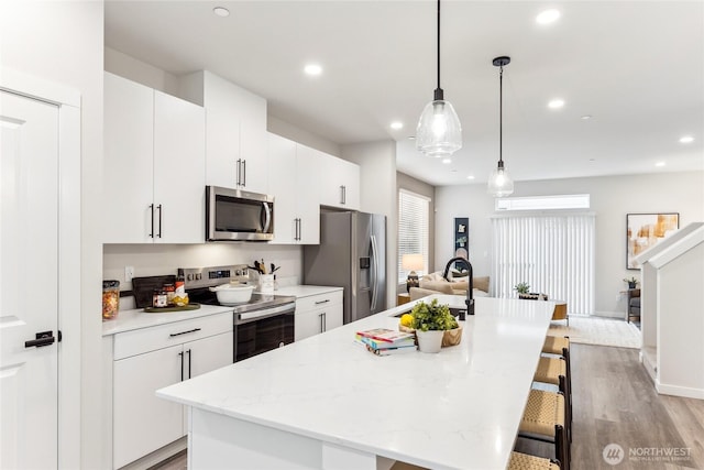 kitchen featuring a sink, a kitchen breakfast bar, light wood-type flooring, a kitchen island with sink, and appliances with stainless steel finishes
