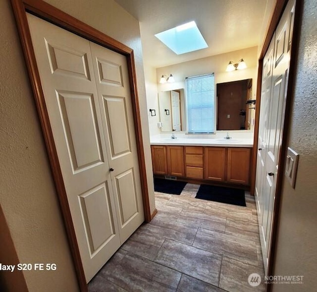 full bath featuring double vanity, a sink, a textured wall, and a skylight