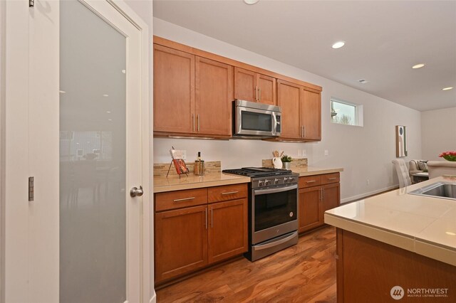 kitchen with light countertops, wood finished floors, appliances with stainless steel finishes, brown cabinetry, and recessed lighting