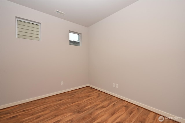 unfurnished room featuring baseboards, visible vents, and wood finished floors