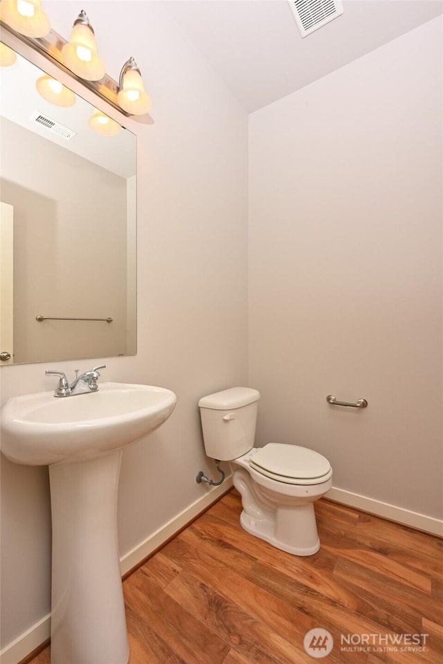 half bathroom with baseboards, visible vents, wood finished floors, and toilet