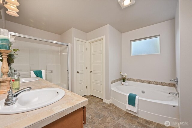 bathroom with a shower stall, double vanity, a sink, and a garden tub