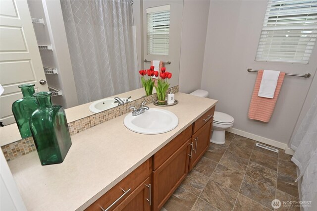 bathroom with vanity, toilet, baseboards, visible vents, and stone finish flooring