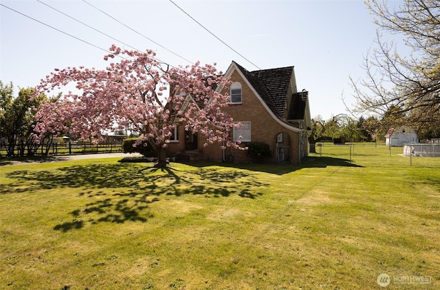 view of side of home featuring brick siding, fence, and a yard