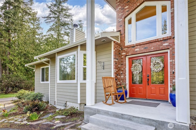 view of exterior entry featuring a chimney, french doors, and brick siding