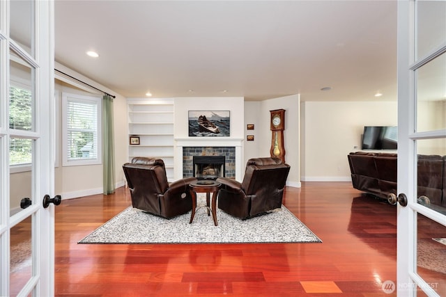 living area featuring baseboards, a fireplace, wood finished floors, and french doors