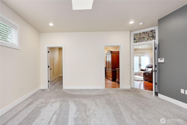 unfurnished bedroom with connected bathroom, carpet, a skylight, baseboards, and recessed lighting