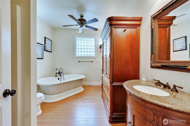 full bath featuring baseboards, ceiling fan, wood finished floors, vanity, and a freestanding bath