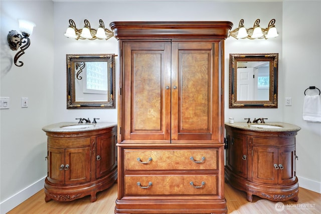 full bath with baseboards, wood finished floors, two vanities, and a sink