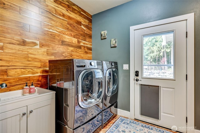 clothes washing area with wood walls, baseboards, light wood-style floors, cabinet space, and washer and clothes dryer