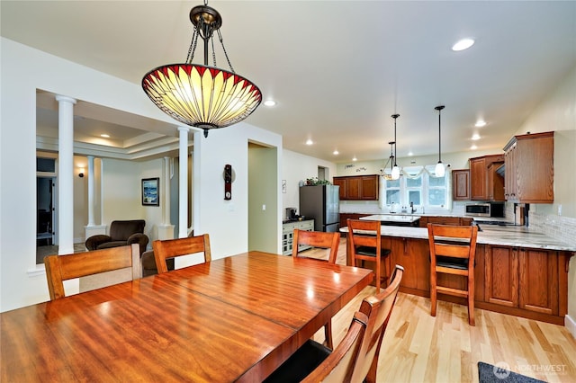 dining space featuring a raised ceiling, recessed lighting, light wood-style floors, and ornate columns