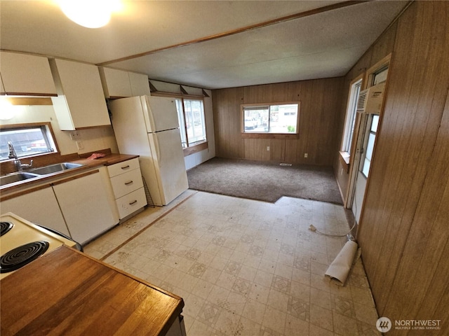 kitchen with freestanding refrigerator, a sink, white cabinetry, wood walls, and light flooring