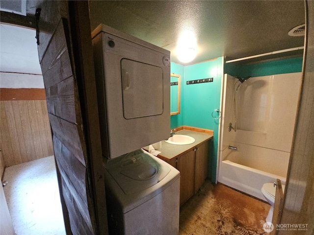 bathroom featuring toilet, estacked washer and dryer, washtub / shower combination, vanity, and a textured ceiling