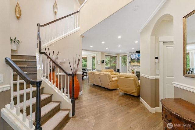 stairs with plenty of natural light, recessed lighting, arched walkways, and wood finished floors