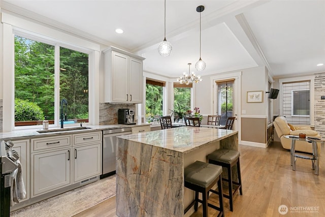 kitchen featuring light stone countertops, a sink, dishwasher, a center island, and ornamental molding