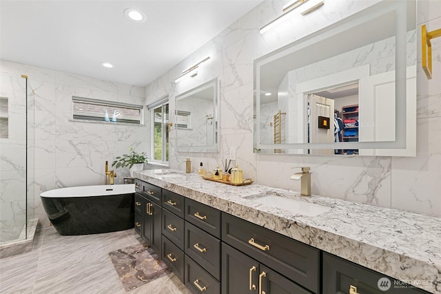 bathroom with double vanity, a freestanding bath, tile walls, a sink, and marble finish floor
