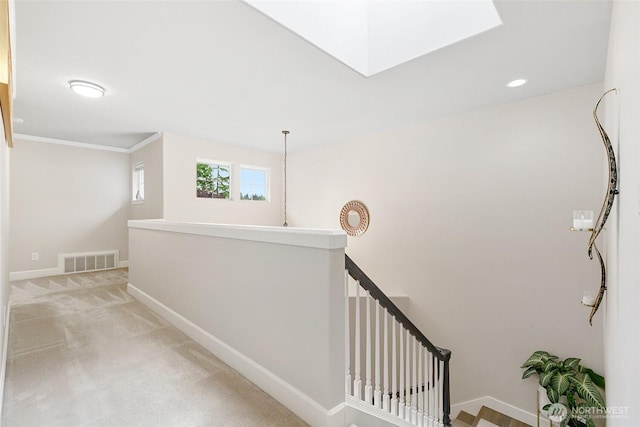 hallway featuring light colored carpet, a skylight, visible vents, baseboards, and an upstairs landing