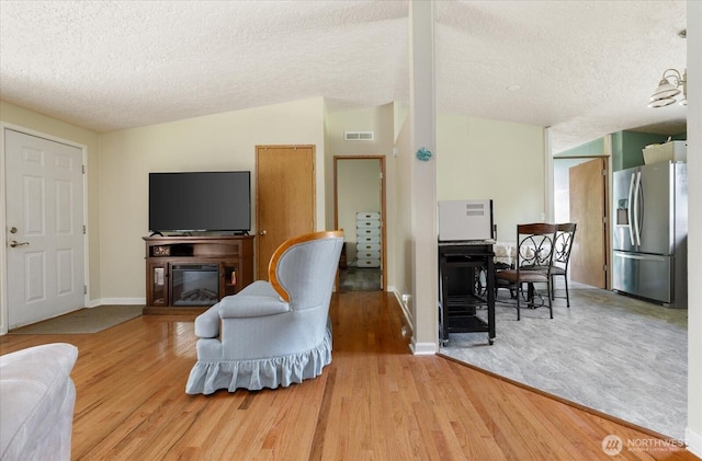 living area featuring visible vents, a textured ceiling, a glass covered fireplace, and wood finished floors