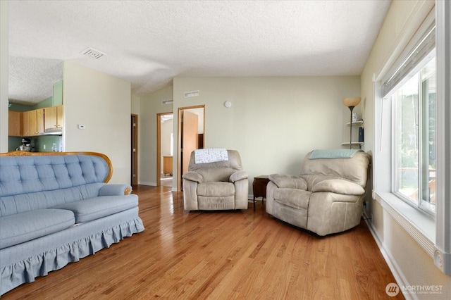 living room with light wood-type flooring, a textured ceiling, baseboards, and visible vents