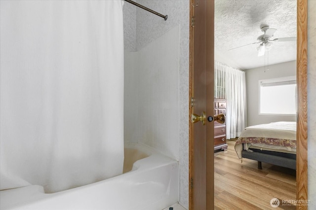 ensuite bathroom with ceiling fan, a textured ceiling, wood finished floors, shower / bath combo with shower curtain, and ensuite bath