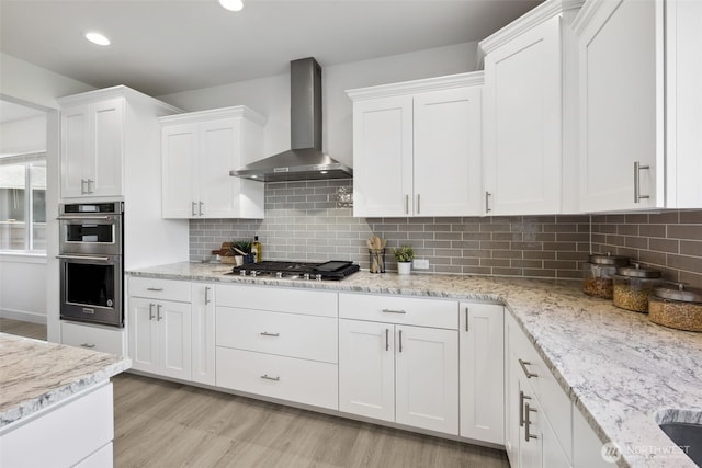 5842 229th Ave E, Buckley, WA 98321 - kitchen with wall chimney range hood, appliances with stainless steel finishes, white cabinetry, light wood-style floors, and backsplash