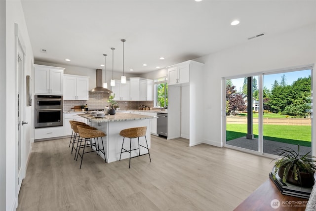 5842 229th Ave E, Buckley, WA 98321 - kitchen featuring appliances with stainless steel finishes, wall chimney range hood, tasteful backsplash, a center island, and light wood-style flooring