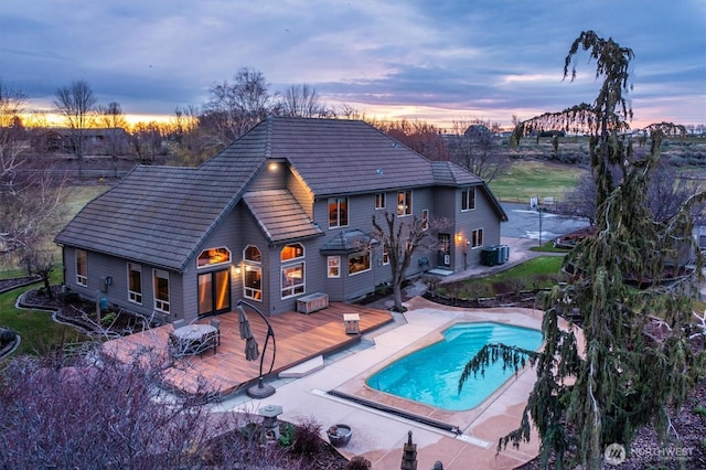 back of property at dusk with central AC unit, a tile roof, a wooden deck, and an outdoor pool