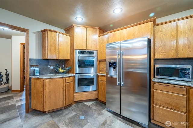 kitchen featuring brown cabinetry, light stone countertops, backsplash, and stainless steel appliances