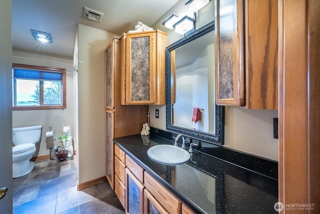bathroom featuring toilet, stone finish flooring, vanity, baseboards, and visible vents